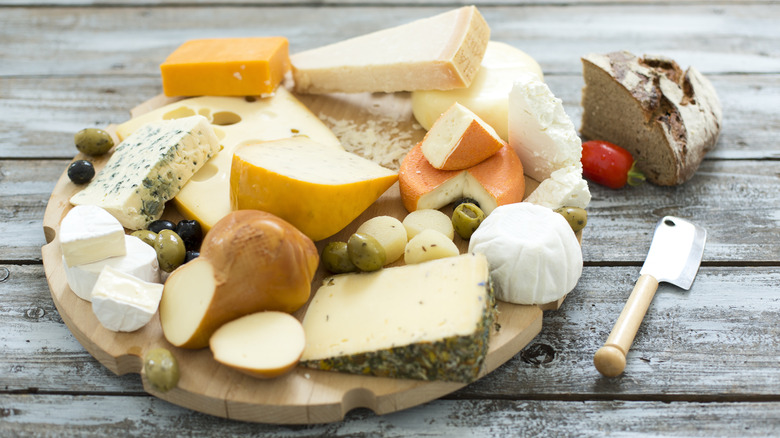 A wooden board containing various firm and soft cheeses