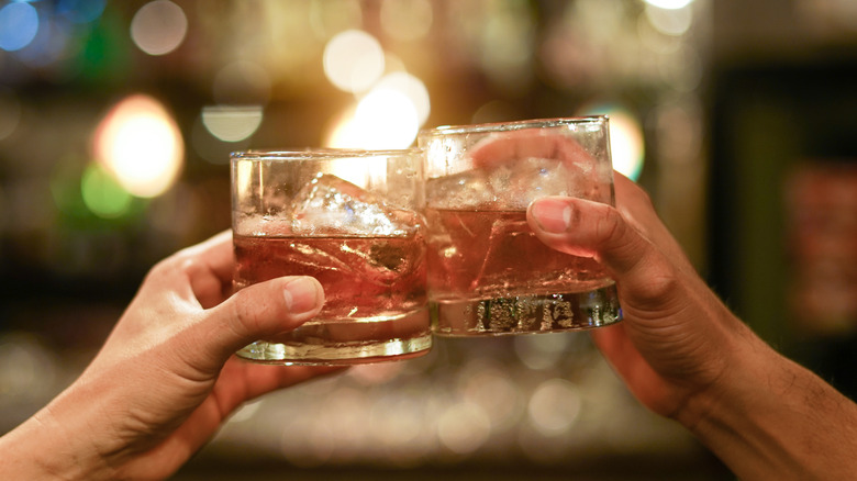 Two people drinking bourbon on the rocks clink their glasses together