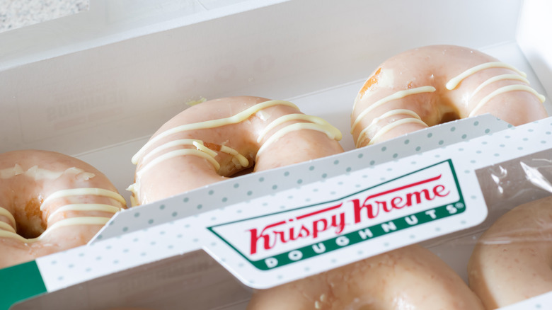 Three iced donuts next to a Krispy Kreme box of more donuts