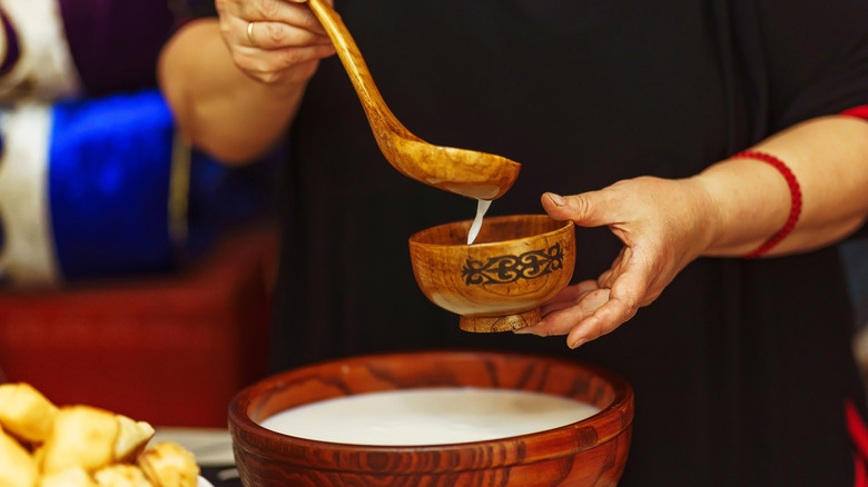 person spoons kumis into a small traditional wooden bowl