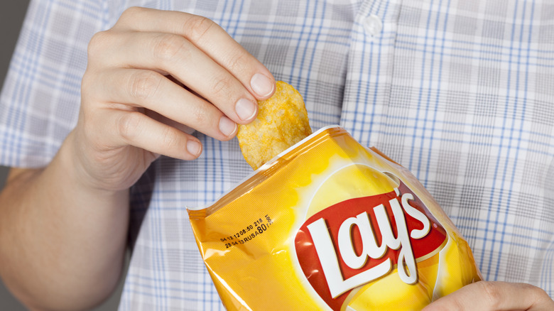 A close up of a person pulling a cheddar and sour cream chip out of a Lay's bag