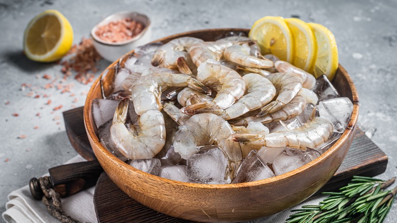Bowl of raw shrimp with tails, lemon, and rosemary