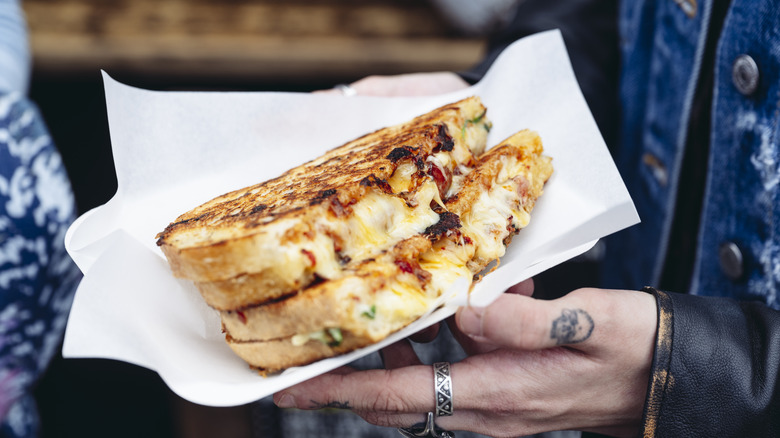 Person holding grilled cheese with peppers and meat