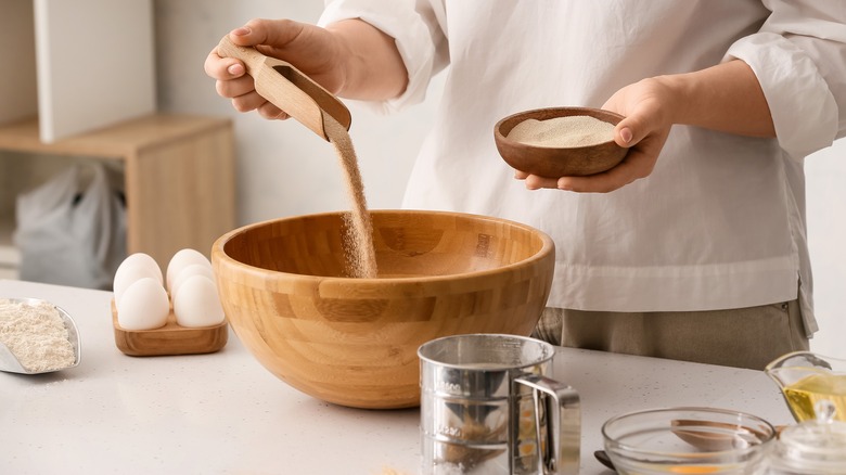 person making bread, pouring yeast in a wooden mixing bowl