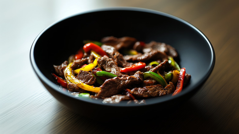 Stir-fried steak with peppers in a black bowl