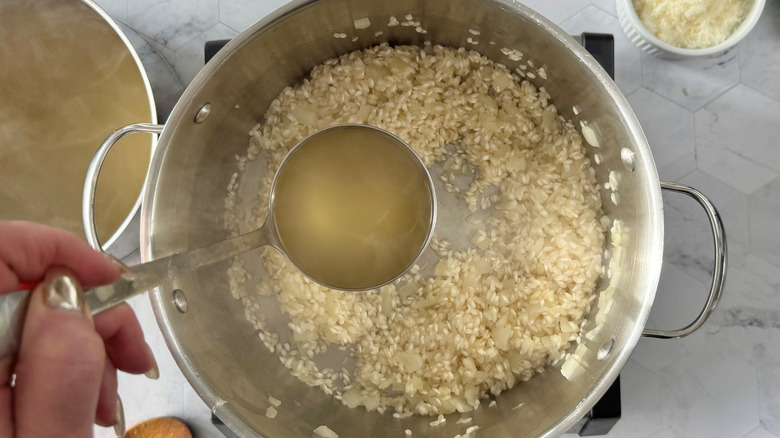 ladling chicken broth into pot with rice