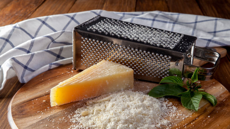 Box grater full of cheese next to parmesan wedge