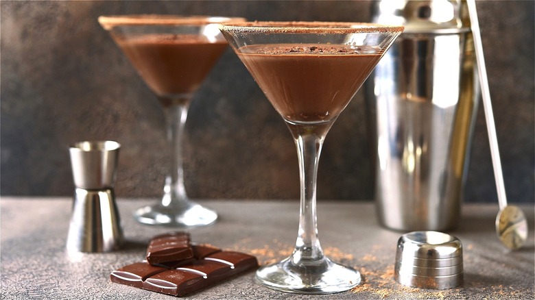 Two chocolate martinis on a gray surface with a broken chocolate bar and cocktail shaker