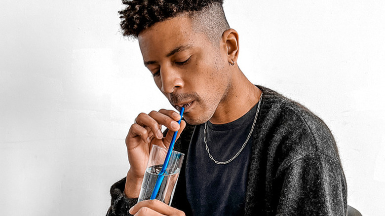 Man drinks from clear glass with Blue Carbon seaweed straw