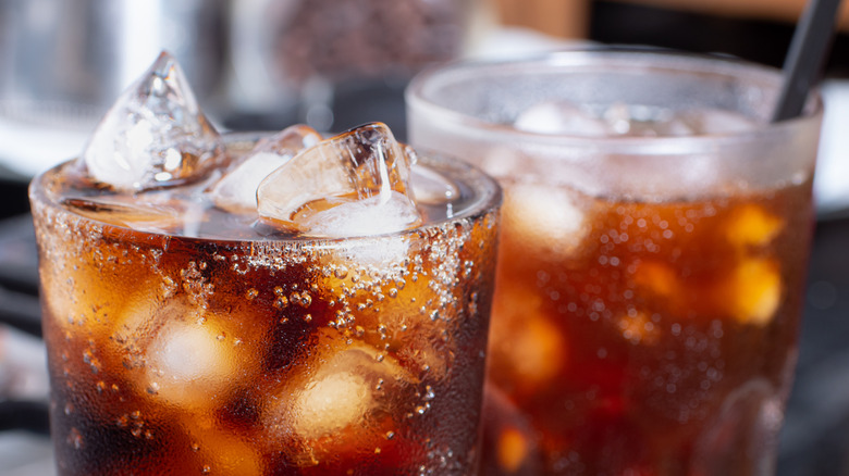 Close up of two glasses of brown soda over ice, one with a straw