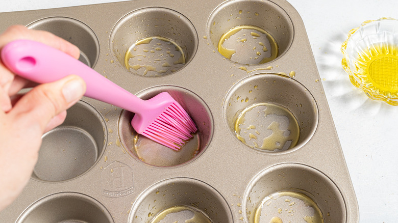 Brushing a muffin pan with oil using a pink pastry brush
