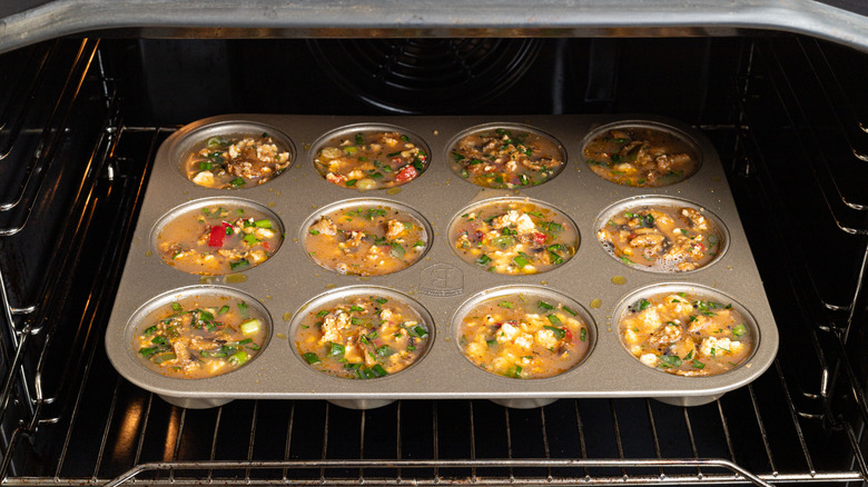 Muffin pan with mushroom egg mixture inside an oven ready to be baked