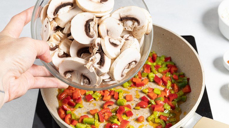 Adding mushrooms to a skillet with bell peppers in it