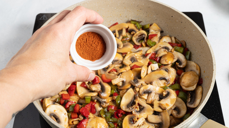Adding paprika to a skillet with mushrooms and bell peppers