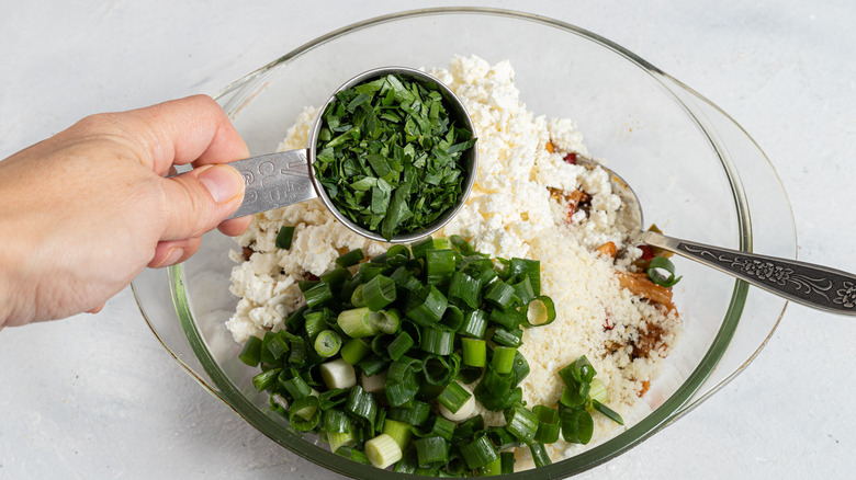 Adding chopped fresh parsley to a bowl with green onion, feta and parmesan