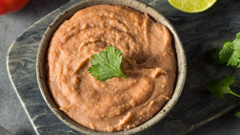 a bowl of refried beans with cilantro garnish on a wooden surface