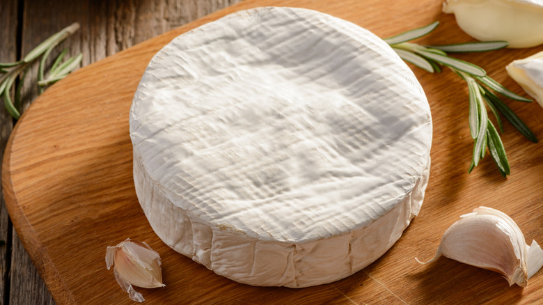Wheel of brie with garlic and rosemary on cutting board