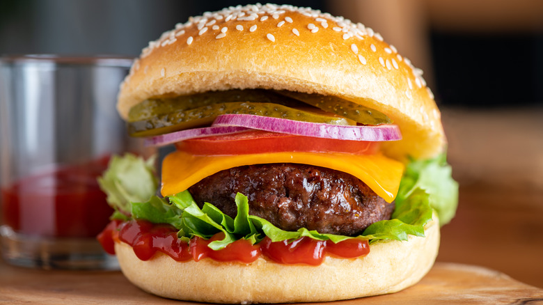 A homemade cheeseburger on a sesame bun with pickles, onion, tomato, lettuce, and ketchup