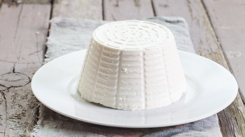 Some ricotta cheese shaped like its round container sits on a white plate.