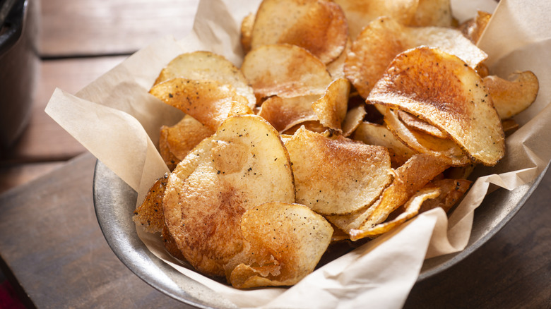 A basket of golden brown homemade seasoned potato chips sits on a table.