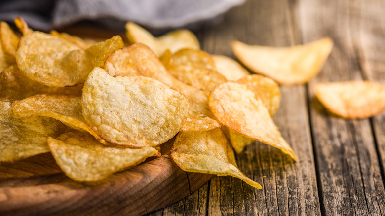 Crispy potato chips sit on a cutting board.