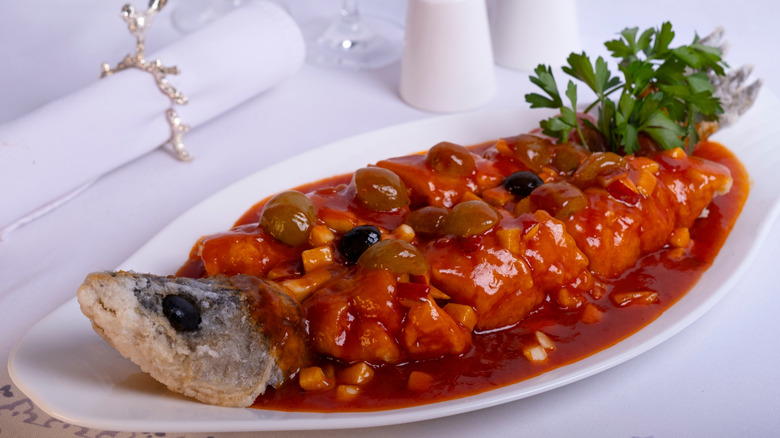 Whole cooked fish with a tomato sauce and parsley garnish