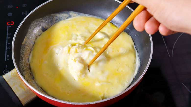 cooking omelet in pan with chopsticks