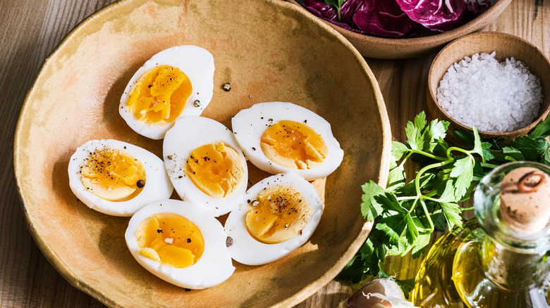 Bowl of boiled eggs surrounded by oil, salt, and herbs