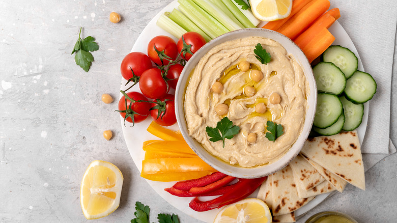 A bowl of hummus with oil and chickpeas on a veggie platter