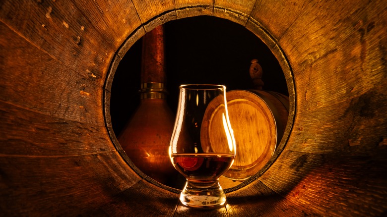 Glass of Scotch whisky in an oak barrel