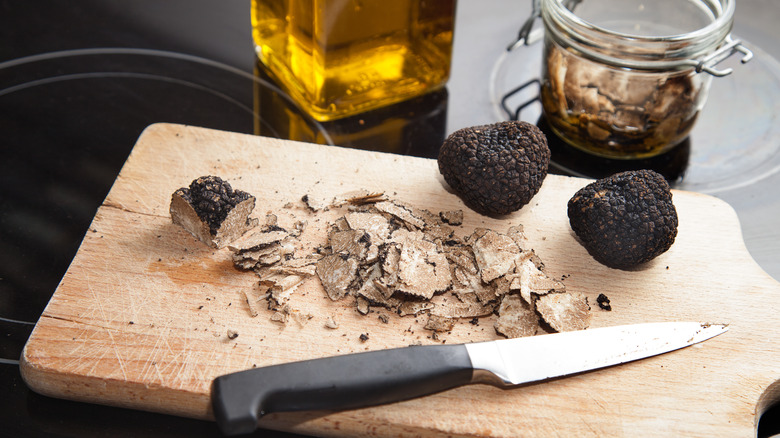 Whole and slices black truffles on cutting board with knife and bottle of oil