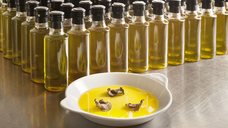 Black truffle shavings in bowl of olive oil with many oil bottles in background