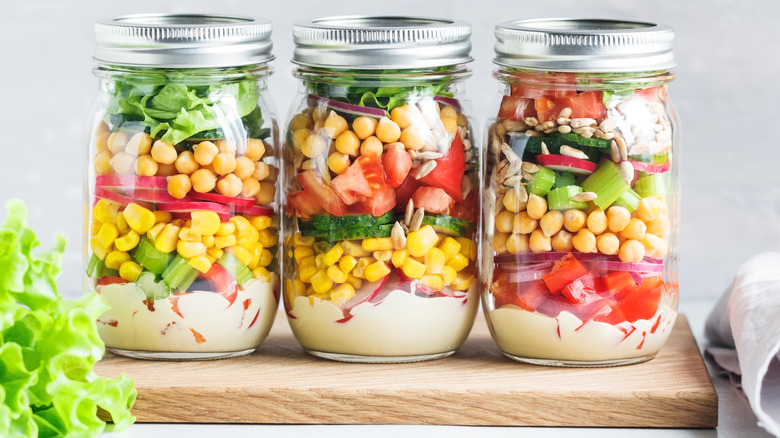 Three mason jars filled with salad ingredients lettuce chickpeas tomatoes corn