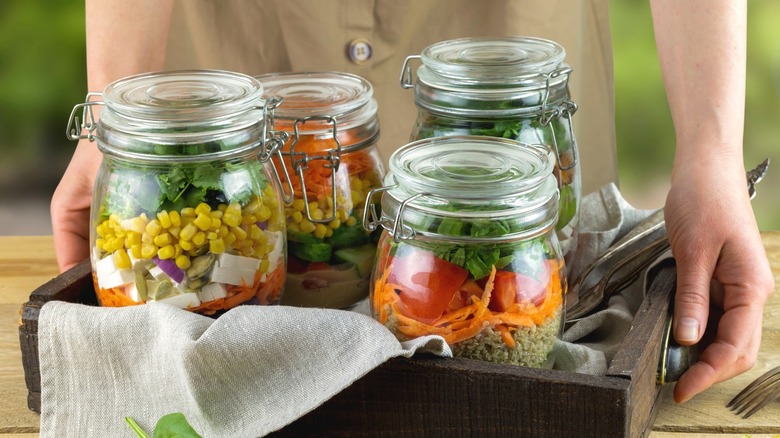 A woman sets down a wood tray with Mason jars filled with salad