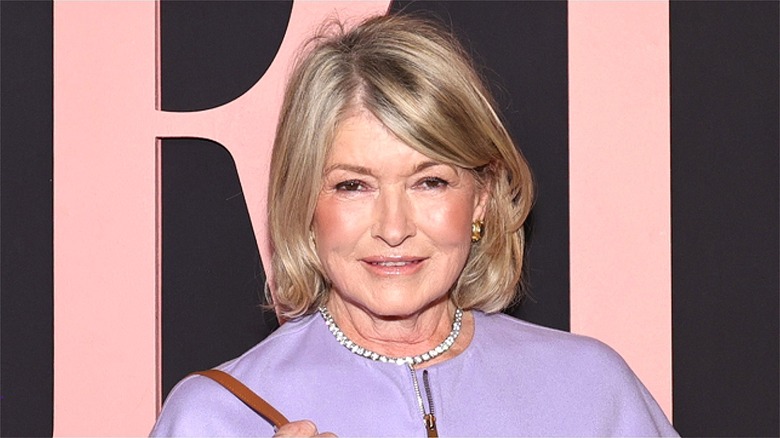 Martha Stewart is smiling and wearing a lavender jacket and gold earrings