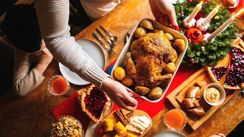 Person holding a cooked turkey over a holiday table setting with candles