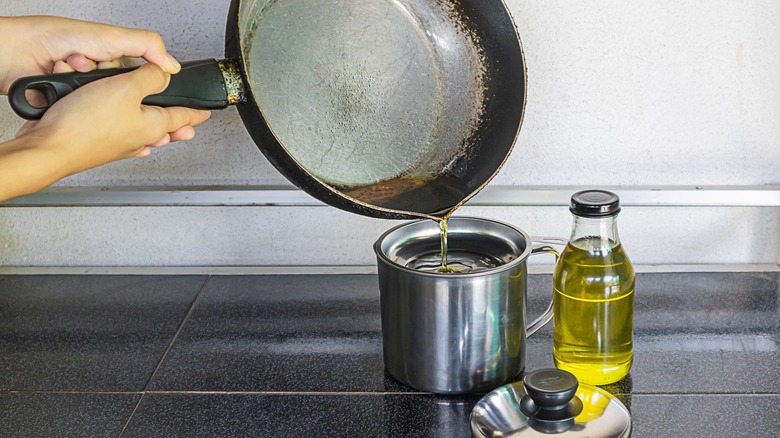 Hands pour used cooking oil from pan into container