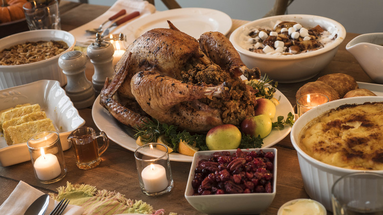 Thanksgiving dinner spread on a table with a turkey surrounded by casseroles, cornbread, and cranberries