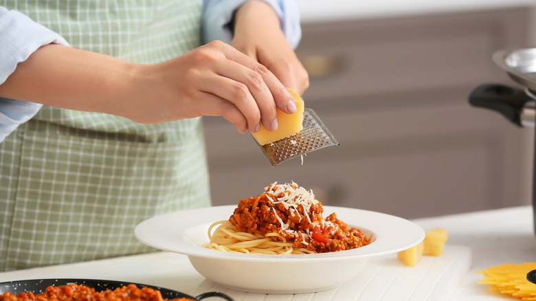 Person grating parmesan on pasta