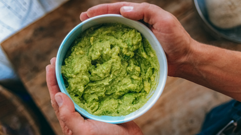 hands holding a bowl of guacamole