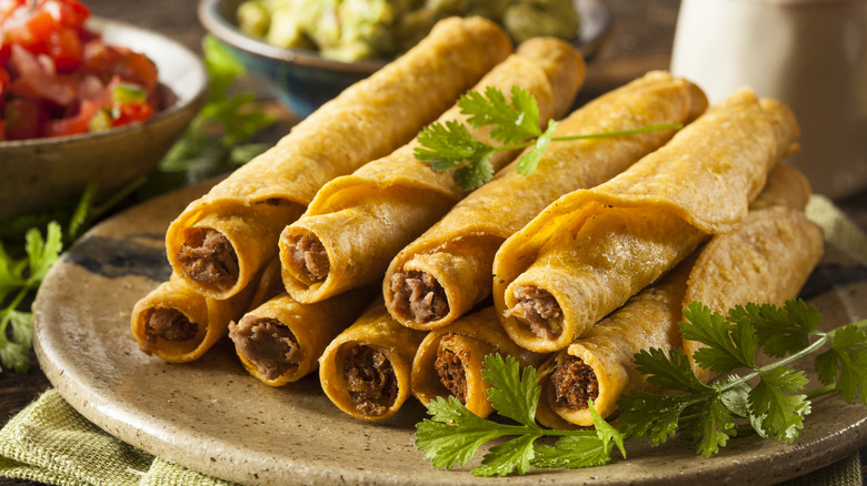 A serving of beef taquitos on a serving platter with cilantro and salsa