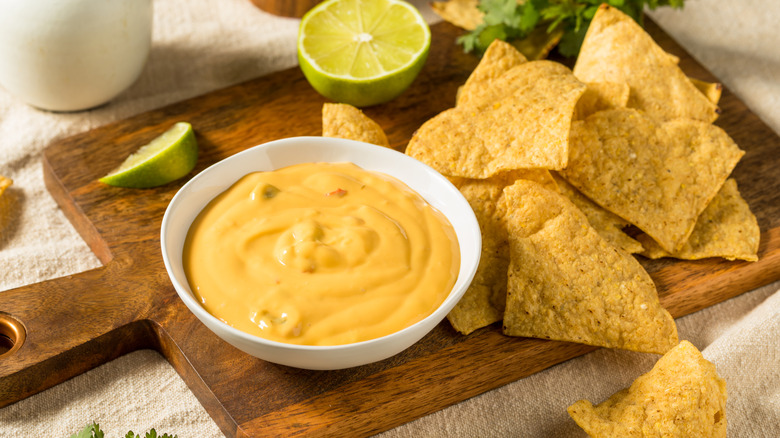 a bowl of queso alongside chips and limes