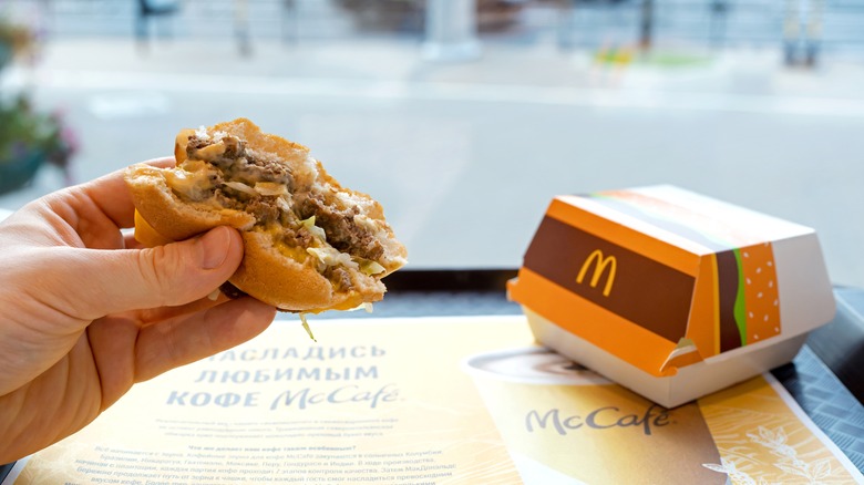 Person holding mostly eaten McDonald's cheeseburger