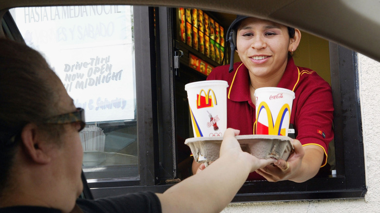 A McDonald's employee hands a cardboard carrier of drinks to a customer through the drive-thru window