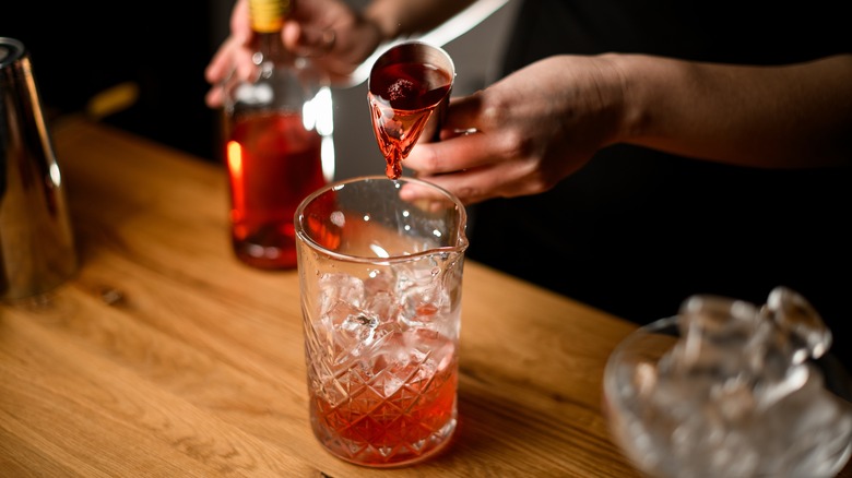 a bartender pouring liquid from a jigger into a measuring glass.