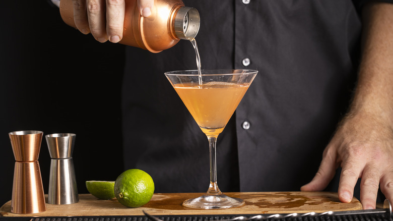 Man pouring orange cocktail out of shaker and into martini glass