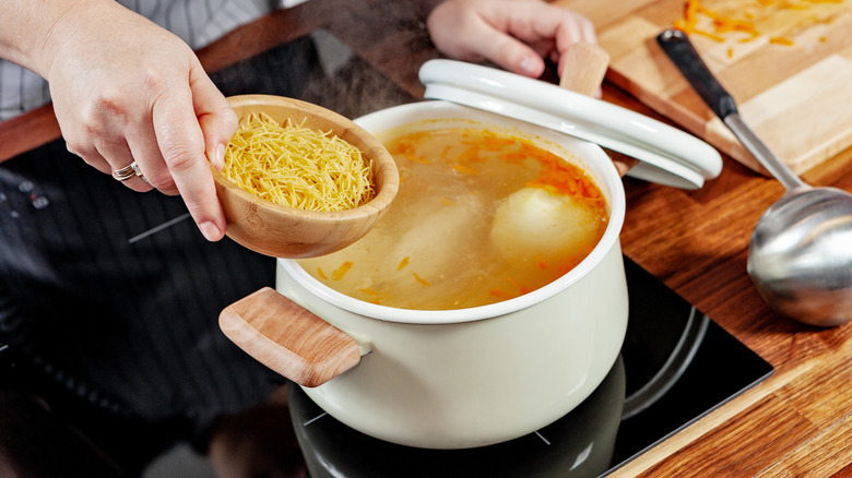 Woman about to pour pasta into soup