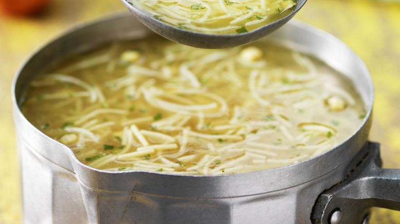 Soup ladle filled with broth and noodles