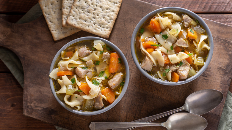 Two bowls of chicken noodle soup with two spoons