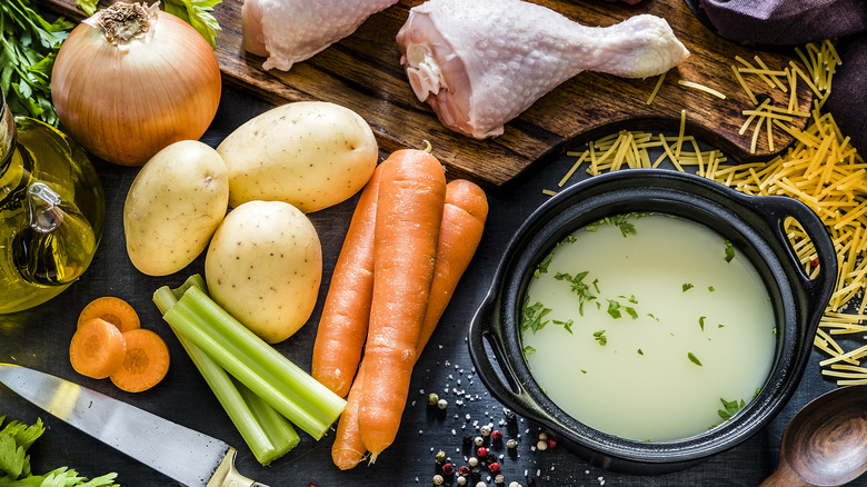 Chicken, onion, potatoes, carrots, celery, noodles and broth next to cutting board